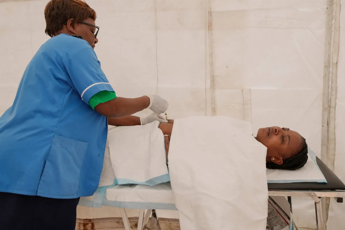 Inside a clinic in Harare, a health worker prepares or gives an injection to a seated patient; posters on the wall and medical supplies on a table are visible.
