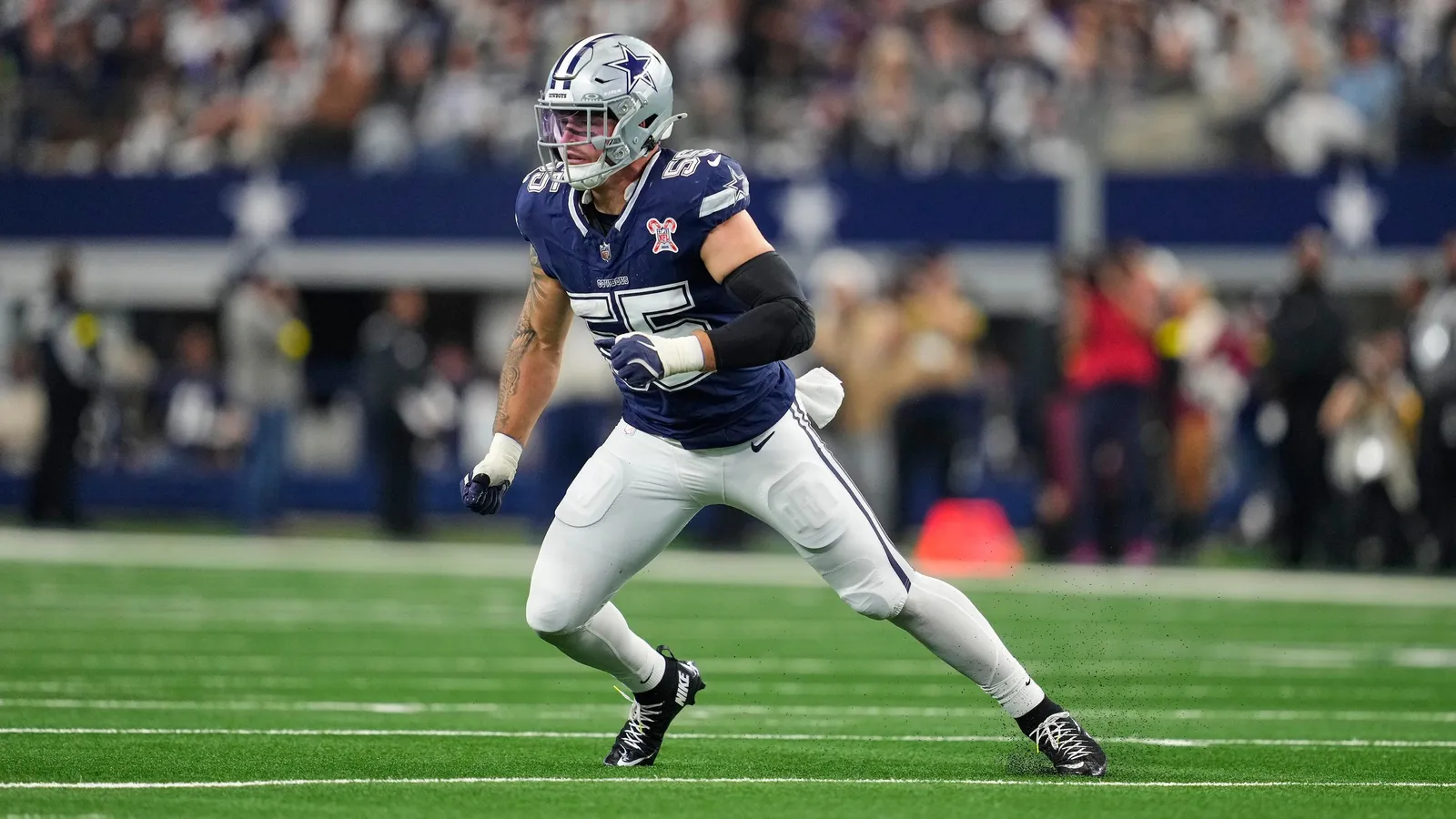 Logan Wilson in a Dallas Cowboys jersey on the sidelines, helmet off, looking toward the field.