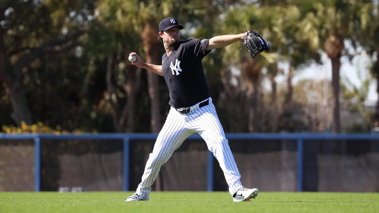 Gerrit Cole in New York Yankees uniform, mid-throw on the mound during a rehab session, stadium seats blurred behind him.